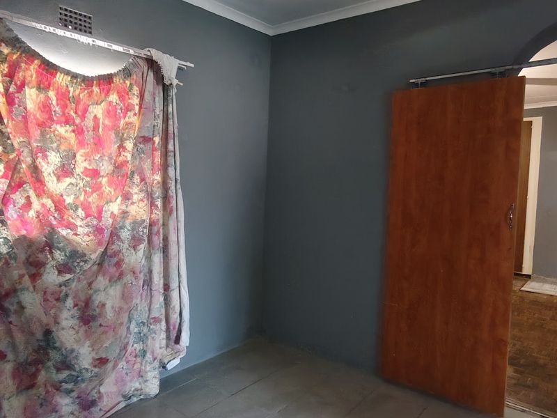 An empty bedroom featuring dark grey walls, a sliding wooden door, and an arched entryway leading to an adjacent room.