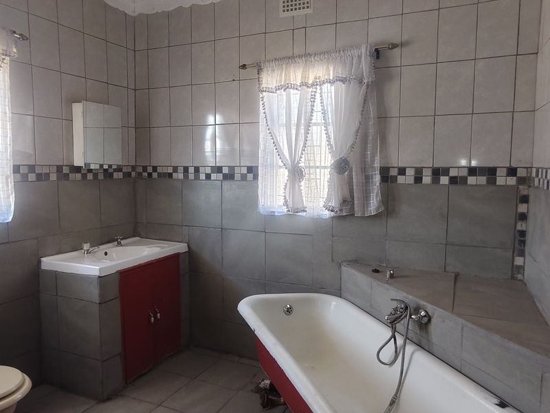A dated bathroom featuring tiled walls, a built-in vanity, a freestanding bathtub, and a standard toilet.