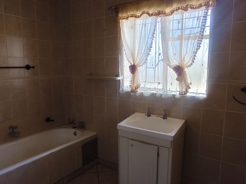 A functional bathroom featuring a built-in bathtub, vanity cabinet, and full-height ceramic wall tiling, offering a neutral base for potential modernization.