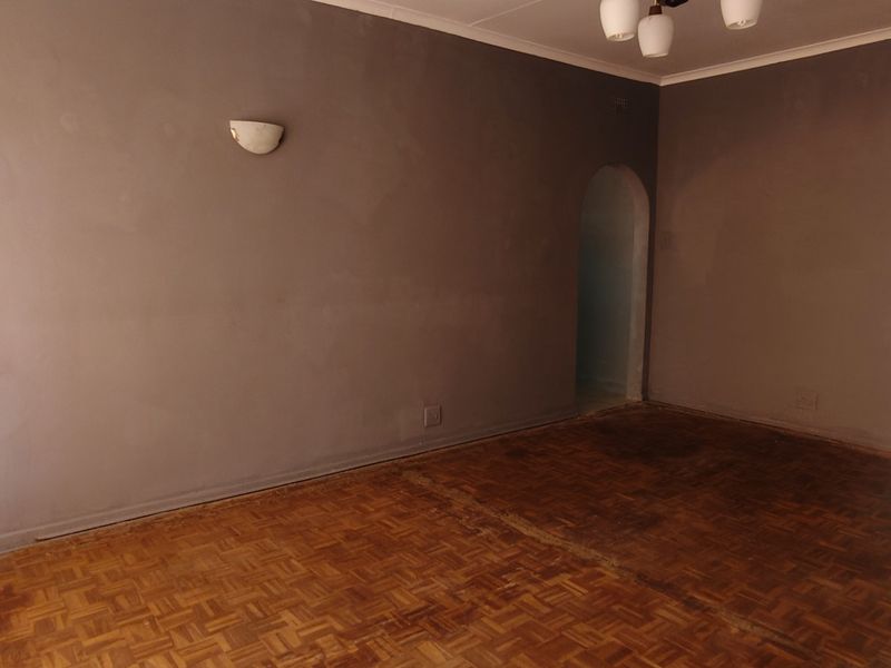 An empty living room featuring original parquet flooring, arched doorways, and neutral wall finishes, offering a blank canvas for renovation or interior design.