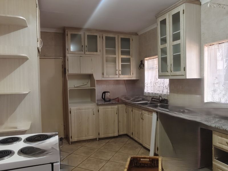A dated kitchen featuring light wood cabinetry, granite countertops, a double sink, and tiled flooring, offering significant potential for a modern renovation.