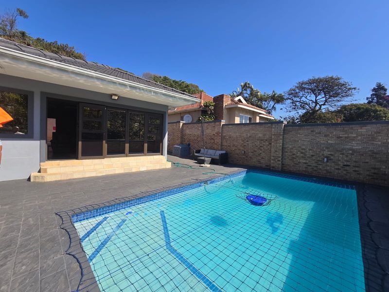 Outdoor pool area featuring a tiled deck, safety net, and direct access to the home through sliding glass doors, enclosed by a brick boundary wall.