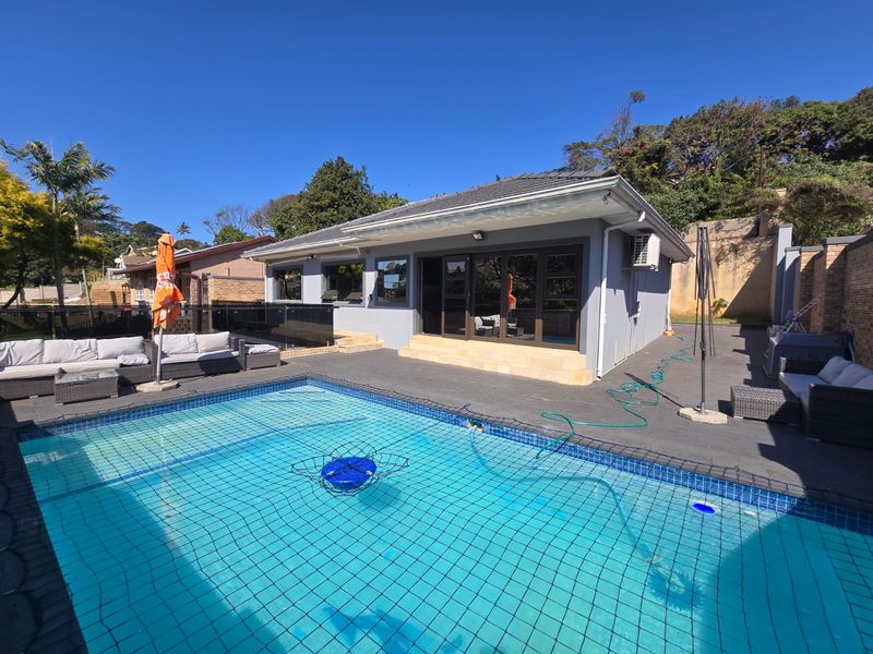 Outdoor pool area featuring a swimming pool with safety net, paved patio space, and direct access to the home via large glass sliding doors.
