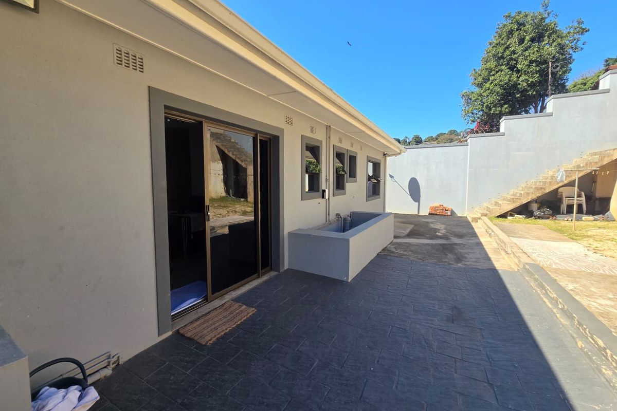 Rear exterior view featuring a paved patio area, sliding glass door access, and concrete retaining wall structure.