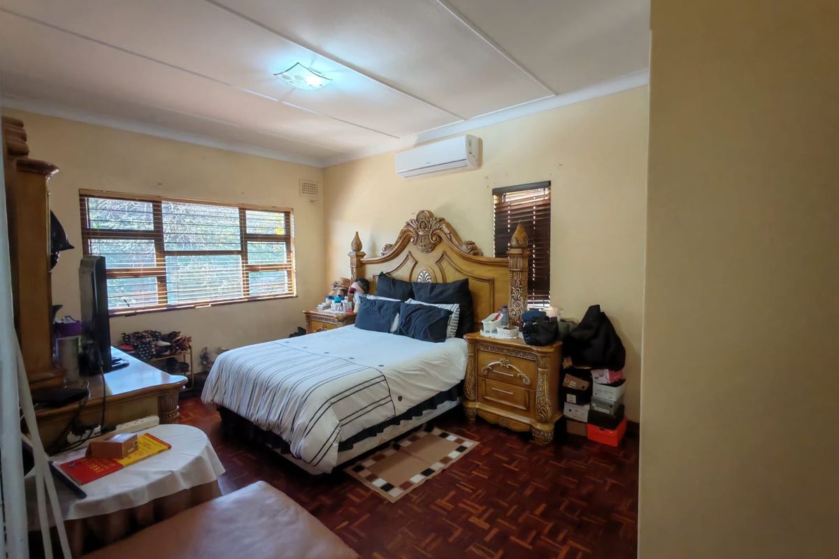 Spacious bedroom featuring parquet flooring, a wall-mounted air conditioning unit, and large windows providing natural light.