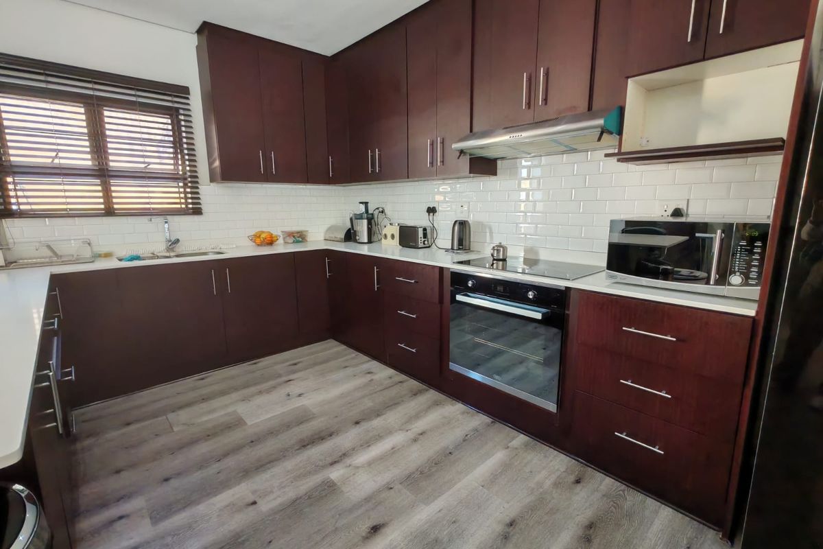 Modern kitchen featuring dark wood cabinetry, white subway tile backsplash, integrated appliances, and durable laminate flooring with ample counter space.