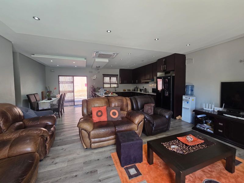 Spacious open-plan living area featuring modern laminate flooring, recessed lighting, and a functional kitchen with dark cabinetry, seamlessly flowing toward the rear entrance.