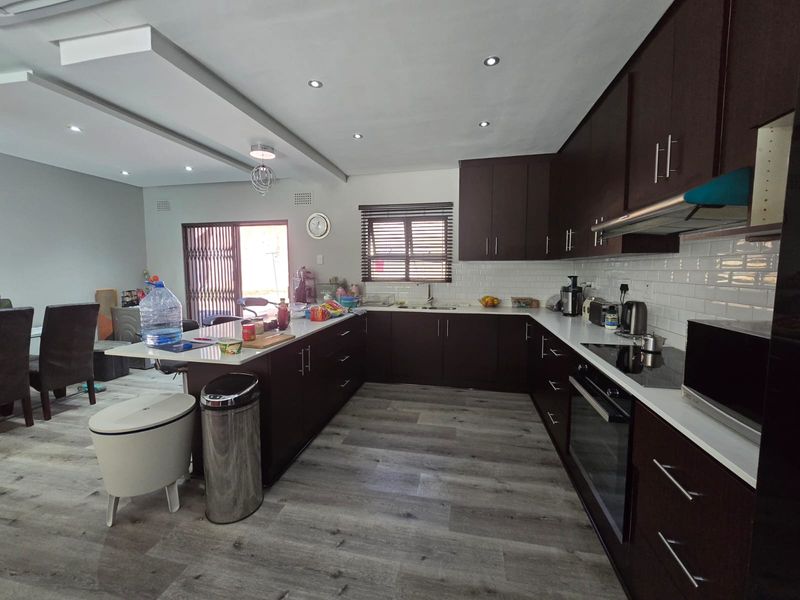 Modern open-plan kitchen featuring dark wood cabinetry, white subway tile backsplash, stone countertops, and integrated appliances, flowing into the dining area.