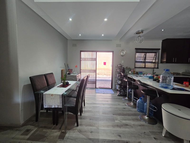 Open plan living and kitchen area featuring modern laminate flooring, recessed ceiling lighting, and a breakfast bar with direct access to the exterior.