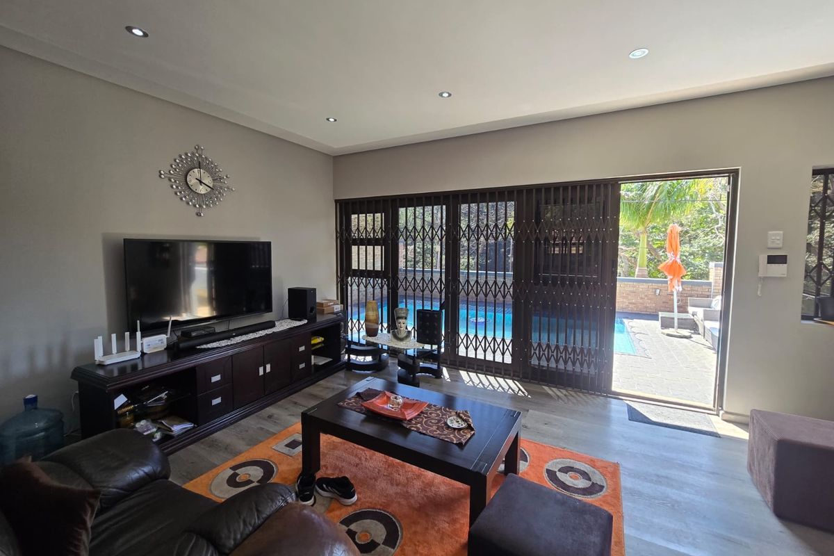 Spacious living room featuring modern laminate flooring, recessed lighting, and large sliding glass doors providing direct access to the outdoor pool area.