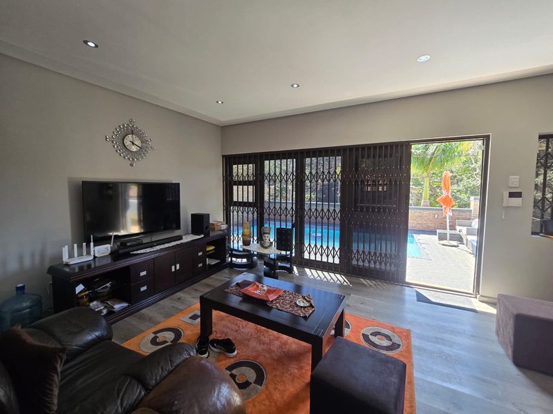 Spacious living room featuring modern laminate flooring, recessed lighting, and large sliding glass doors providing direct access to the outdoor pool area.