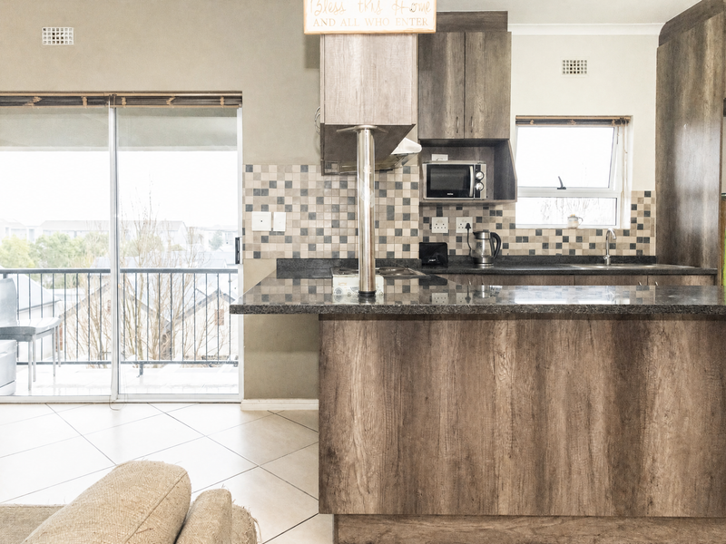 Open plan kitchen and living area featuring granite countertops, wood-look cabinetry, mosaic backsplash, and direct access to a balcony through sliding glass doors.