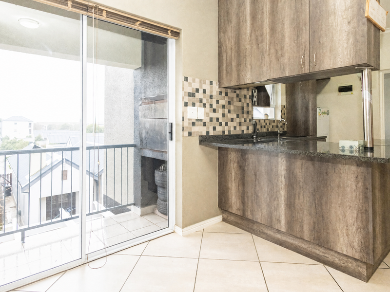 Open-plan kitchen area featuring wood-look cabinetry, granite countertops, and a sliding door leading to a balcony with a built-in braai.
