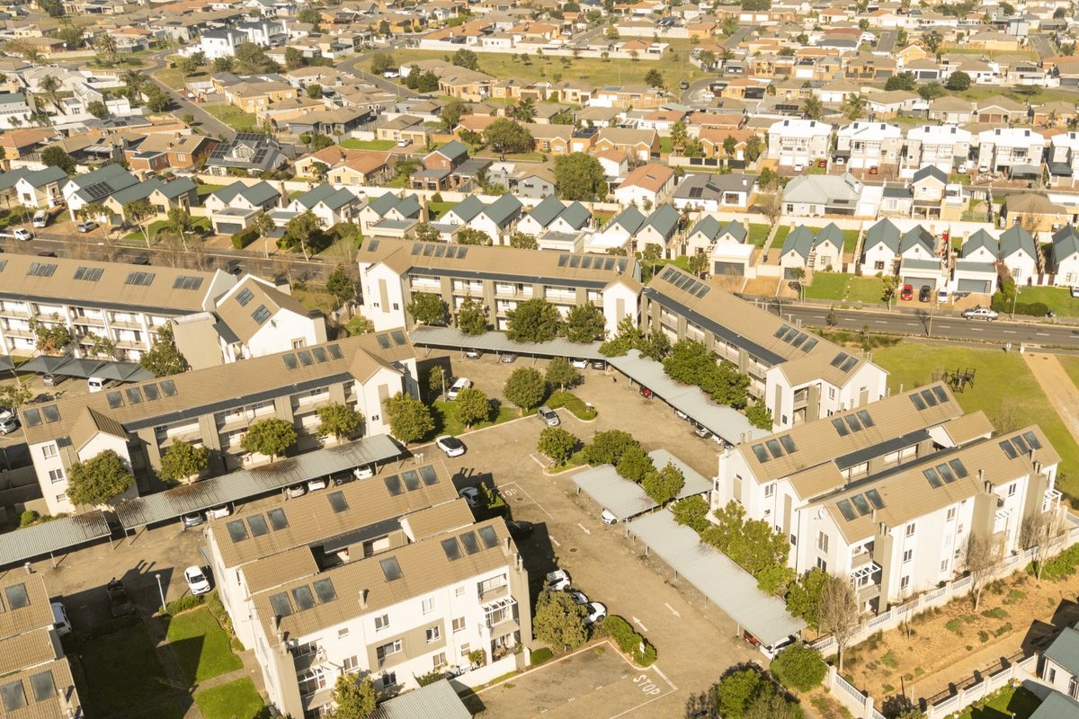 Aerial view of a residential apartment complex featuring multiple buildings, tiled roofs, covered parking areas, and established communal landscaping.