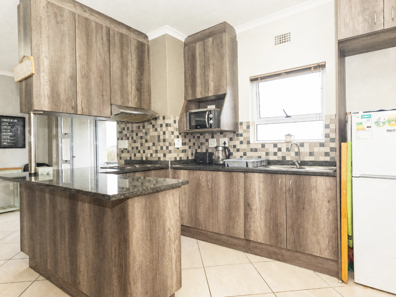 A functional kitchen featuring wood-look laminate cabinetry, granite countertops, a mosaic tile backsplash, and integrated storage space.
