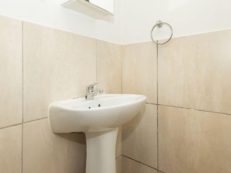A compact bathroom featuring a white pedestal basin with a chrome mixer tap and neutral wall tiling.