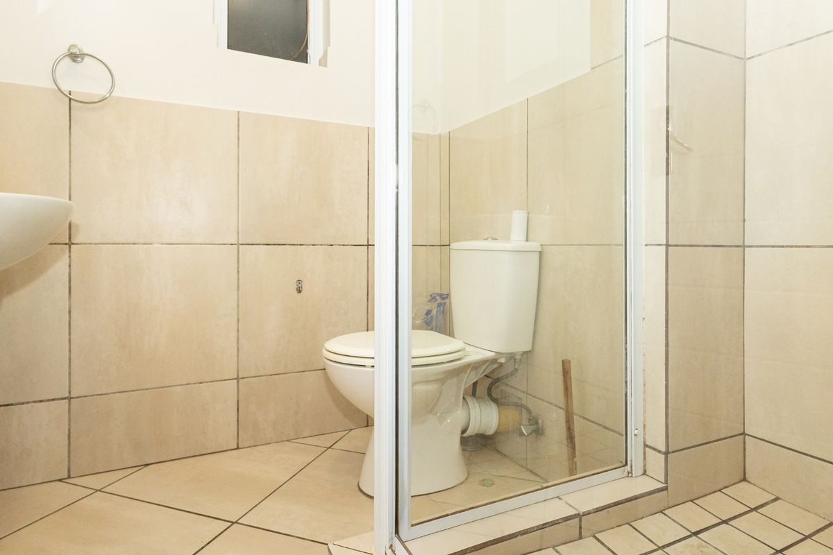 A functional bathroom featuring a pedestal basin, toilet, and a glass-enclosed shower with neutral wall and floor tiling.