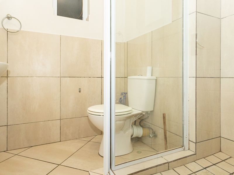 A functional bathroom featuring a pedestal basin, toilet, and a glass-enclosed shower with neutral wall and floor tiling.
