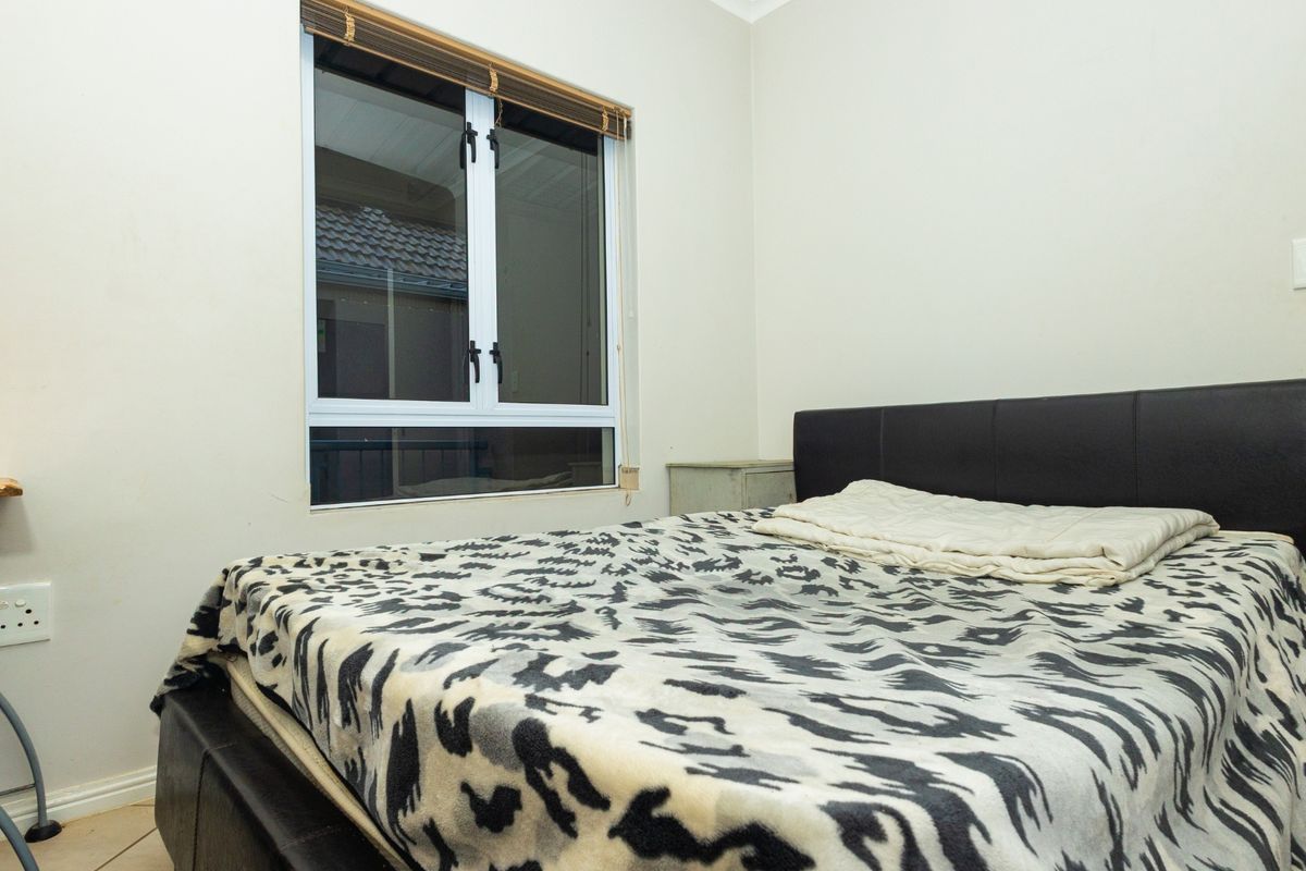 A functional bedroom featuring tiled flooring, a window with fitted blinds, and standard electrical fixtures.