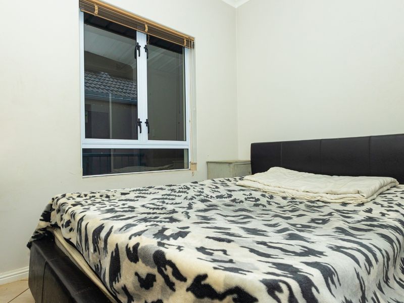 A functional bedroom featuring tiled flooring, a window with fitted blinds, and standard electrical fixtures.