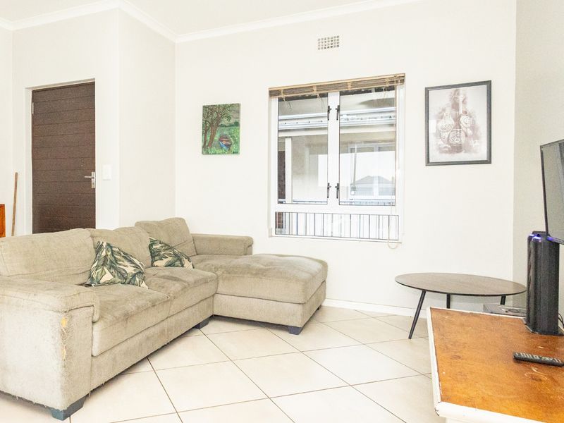 A bright living room featuring neutral tiled flooring, a large window providing natural light, and a functional layout suitable for comfortable seating.