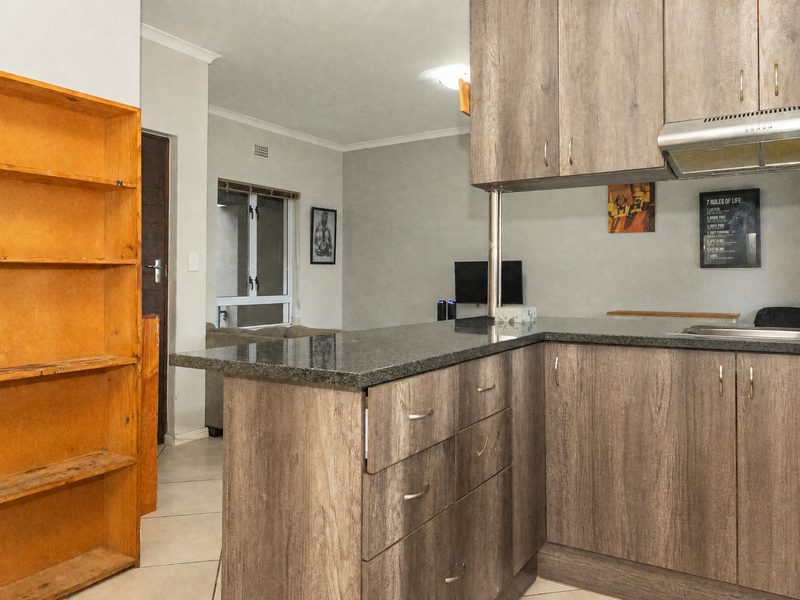 Open plan kitchen featuring wood-look laminate cabinetry, granite countertops, and a stainless steel extractor fan, flowing into the adjacent living area.