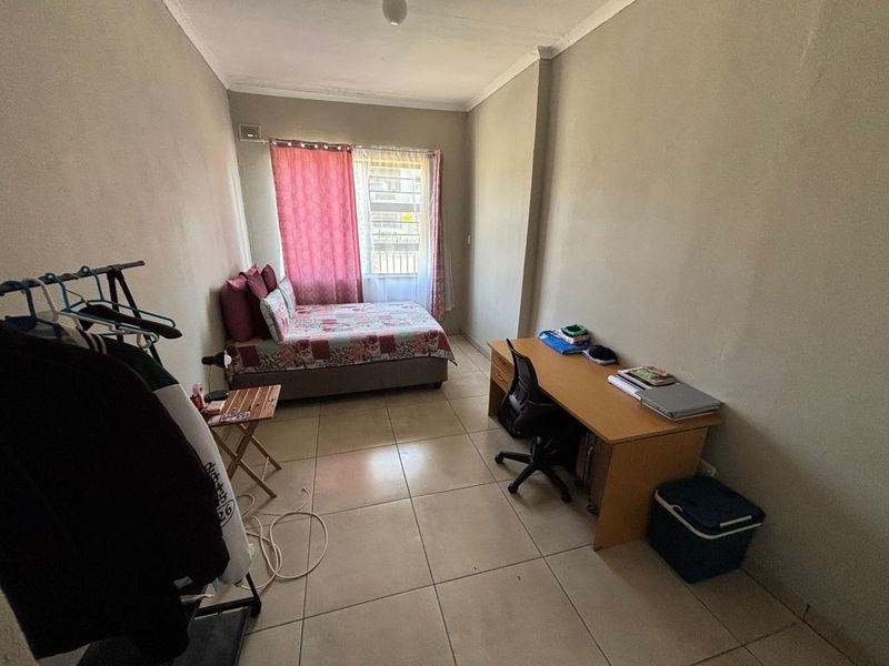 A functional bedroom featuring tiled flooring, a window with security bars, and neutral wall finishes, offering a practical space for rest or study.