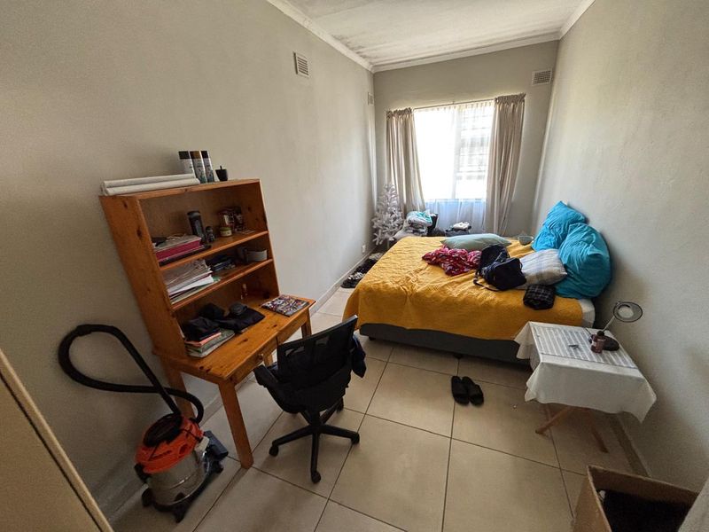 A bedroom featuring tiled flooring and visible ceiling water staining, offering a functional space ready for cosmetic updates.