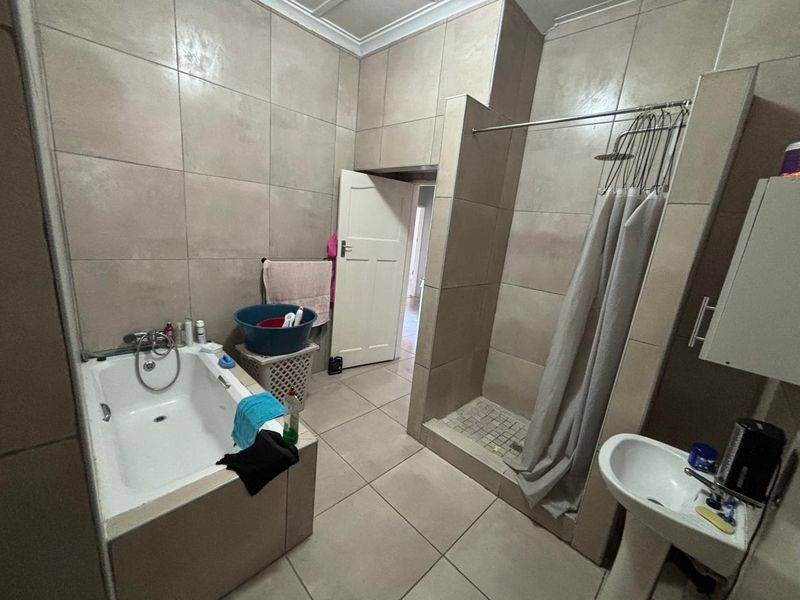 A functional bathroom featuring a built-in bathtub, a walk-in shower with a curtain, and a pedestal basin, finished with neutral ceramic wall and floor tiles.