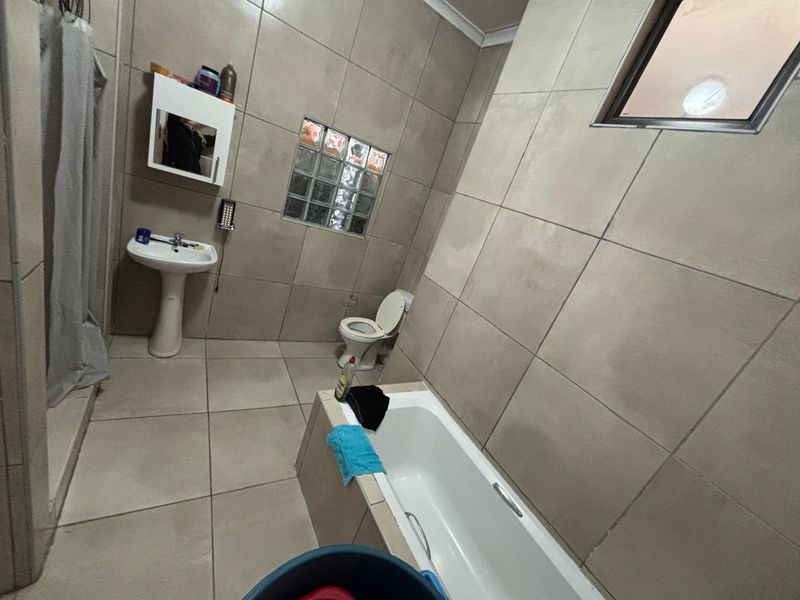 A functional bathroom featuring tiled walls and floors, a pedestal basin, a bathtub, and a toilet, with a glass block window for natural light.
