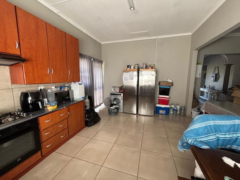 A functional kitchen featuring wooden cabinetry, built-in oven and hob, and tiled flooring with integrated laundry and refrigeration space.