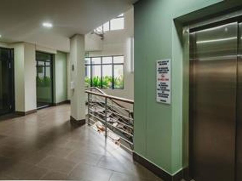 A clean, modern apartment building hallway featuring a stainless steel elevator, tiled flooring, and a staircase with a metal railing.