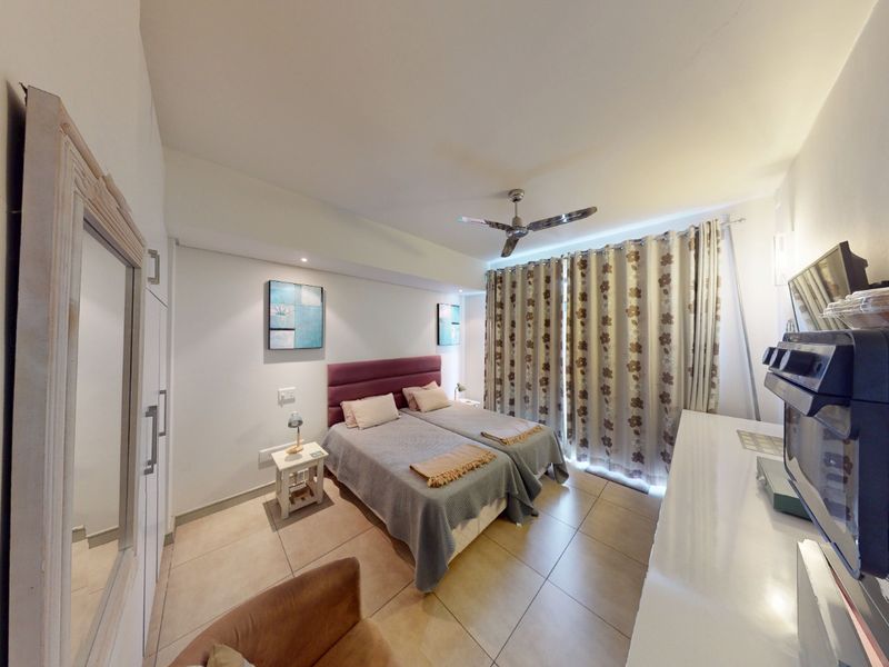 A functional bedroom featuring tiled flooring, a ceiling fan, and built-in storage cupboards, offering a comfortable and practical living space.