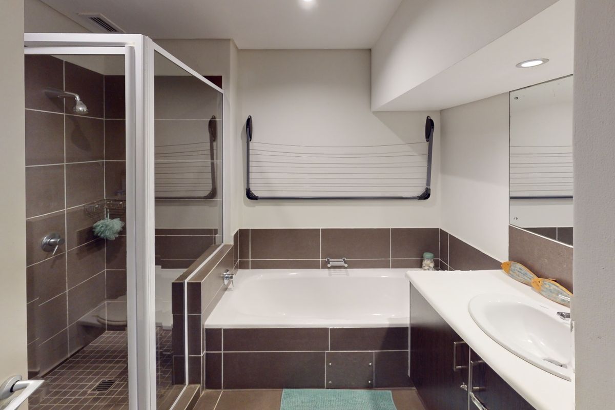 A modern bathroom featuring a glass-enclosed shower, a built-in bathtub with tiled surround, and a vanity unit with an integrated sink.