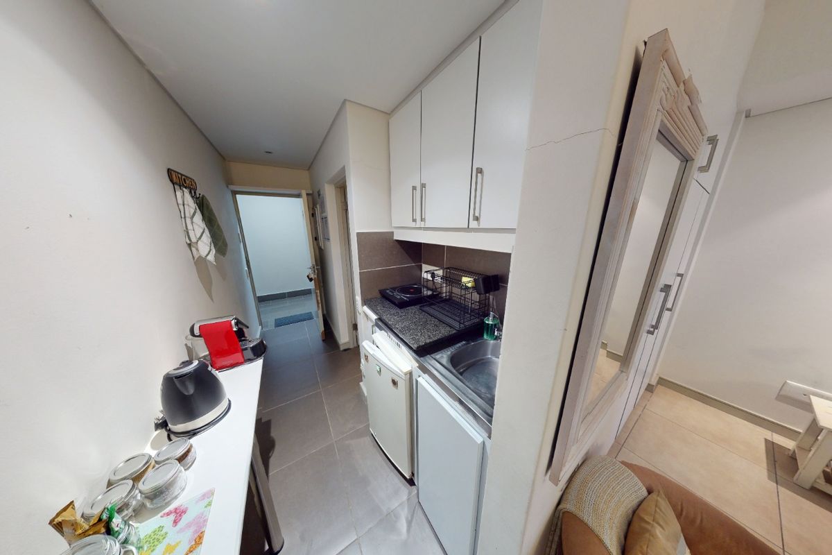 Compact kitchenette featuring built-in cabinetry, granite countertops, and a stainless steel sink, finished with tiled flooring.
