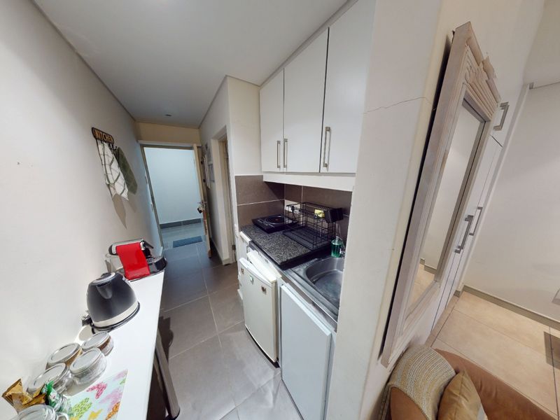Compact kitchenette featuring built-in cabinetry, granite countertops, and a stainless steel sink, finished with tiled flooring.