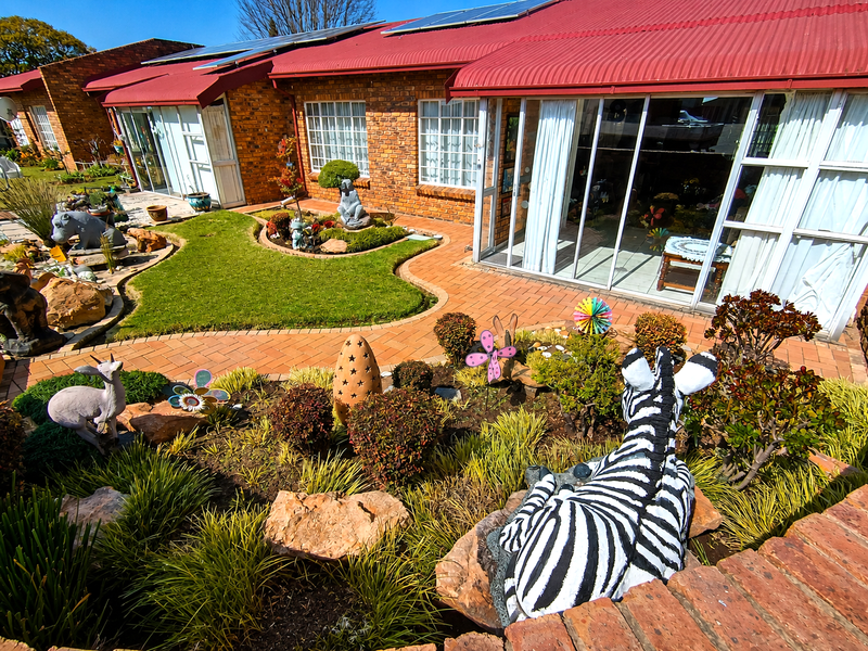 Rear view of a brick apartment building featuring a paved patio area, landscaped garden, and sliding glass doors with solar panels on the roof.