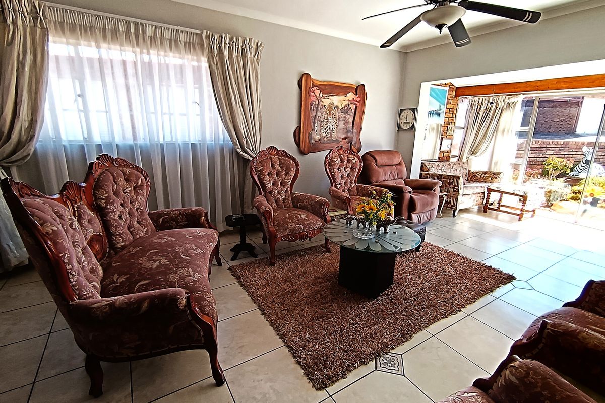 A spacious living room featuring tiled flooring, a ceiling fan, and large windows with natural light, leading to an adjacent patio area.