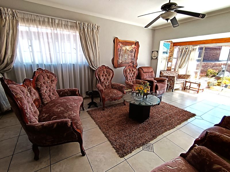 A spacious living room featuring tiled flooring, a ceiling fan, and large windows with natural light, leading to an adjacent patio area.