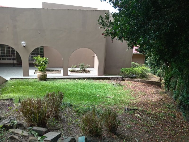 Rear view of the property featuring a covered patio with arched architectural details, overlooking a landscaped garden area with established greenery.