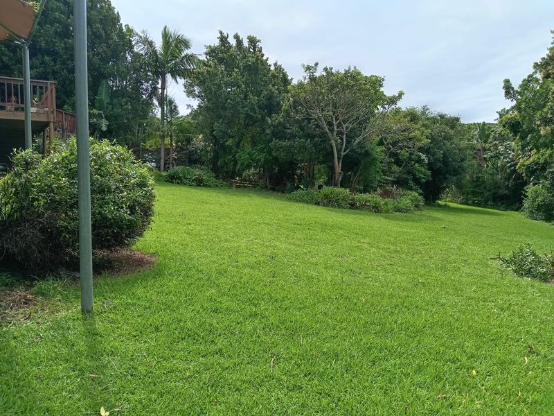 A spacious, well-maintained green lawn surrounded by mature trees and established garden beds, featuring an elevated wooden deck area.