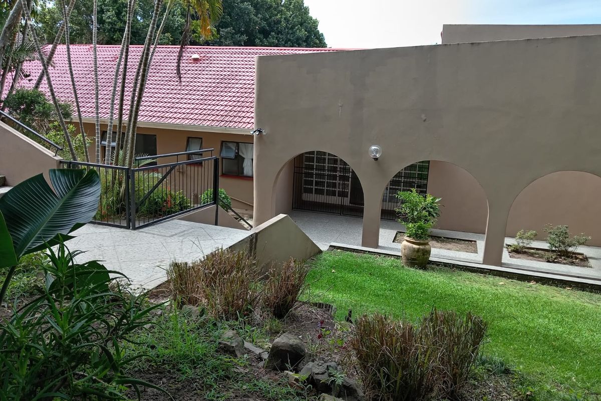 Rear exterior view of the property featuring a covered arched walkway, tiled roof, and landscaped garden area with retaining walls.
