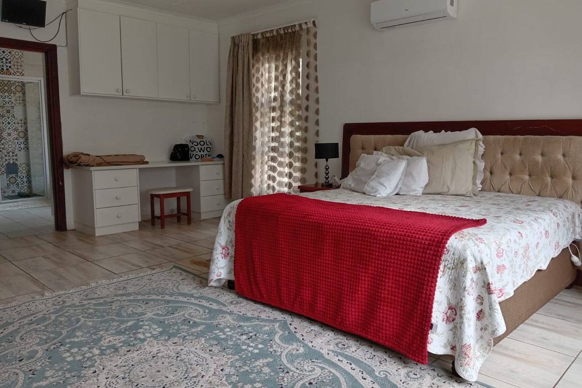 Spacious bedroom featuring built-in cabinetry, a dedicated desk area, tiled flooring, and a wall-mounted air conditioning unit.