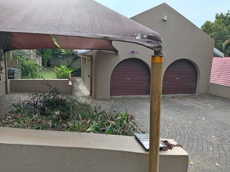 Front exterior view featuring a double garage with roll-up doors, a paved driveway, and a shade sail structure.