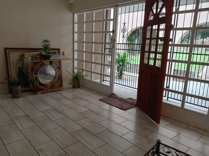 An entrance area featuring light-toned tiled flooring, a timber door, and large glass panels providing a view to the exterior garden.