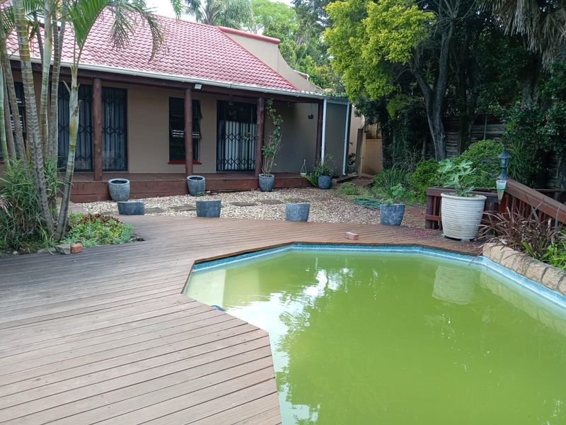 Outdoor pool area featuring timber decking and a swimming pool, adjacent to a covered patio with a tiled roof and security gates.