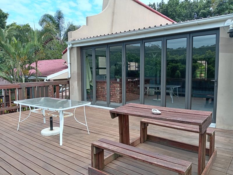 Spacious timber deck featuring a built-in brick braai and large aluminium folding doors providing seamless indoor-outdoor flow.