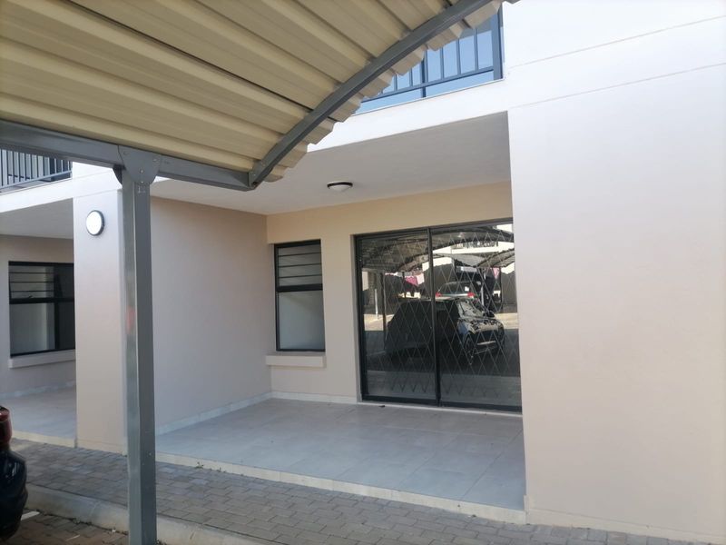Front entrance of the apartment featuring a covered carport, tiled patio area, and a sliding glass door with security gate.