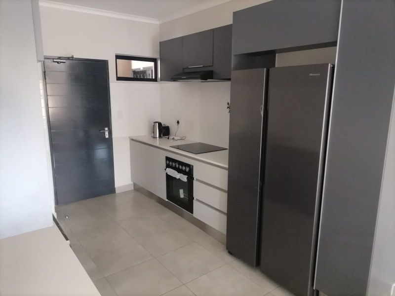Modern kitchen featuring sleek grey cabinetry, built-in oven, electric hob, extractor fan, and neutral tiled flooring.