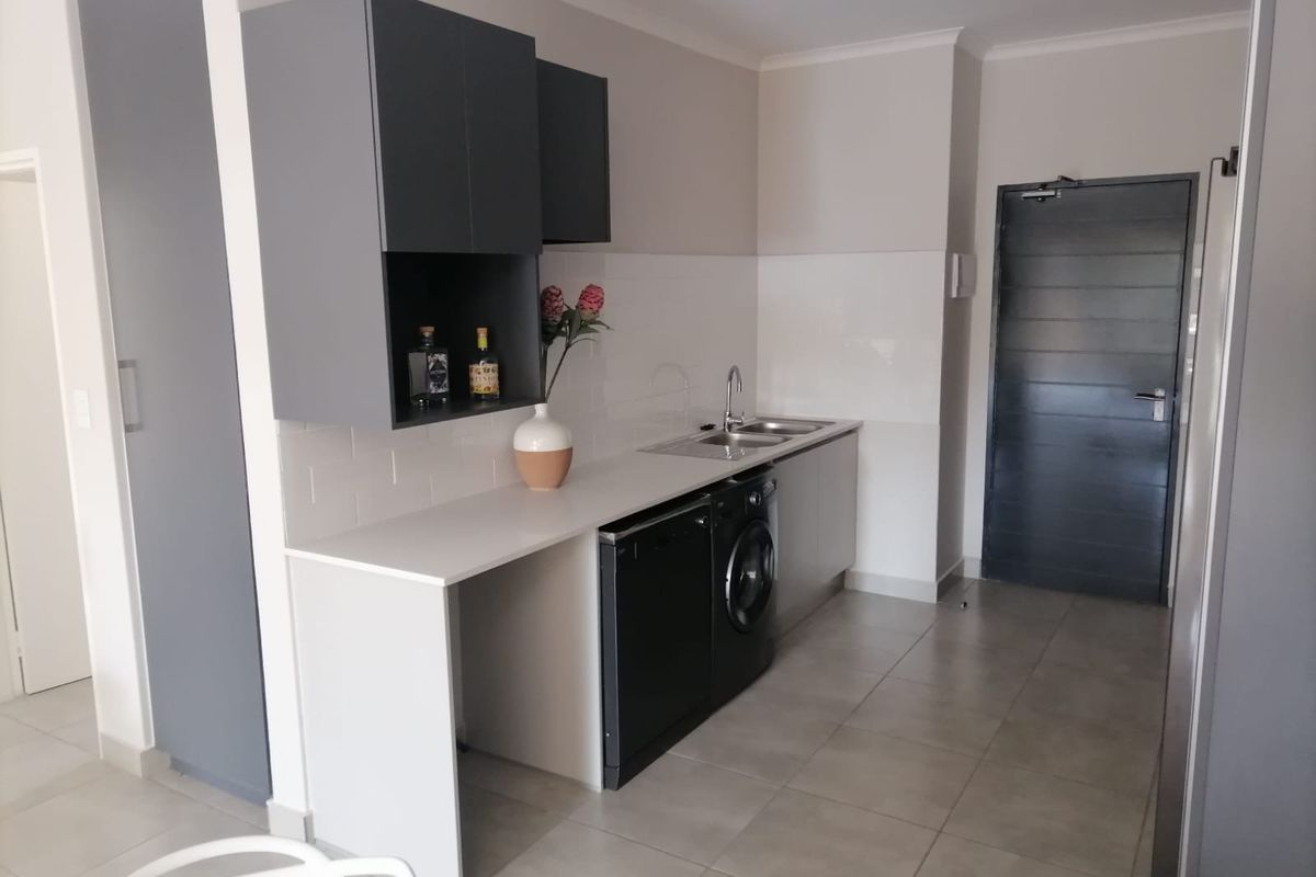 Modern kitchen area featuring sleek grey cabinetry, subway tile backsplash, tiled flooring, and integrated laundry and dishwasher appliances.